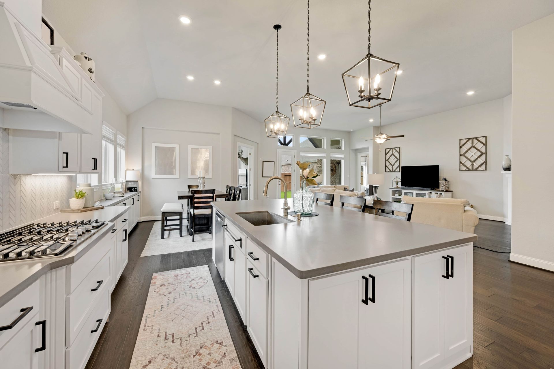 Spacious white kitchen with large island, gray countertop, and dark accents, opening to living area.