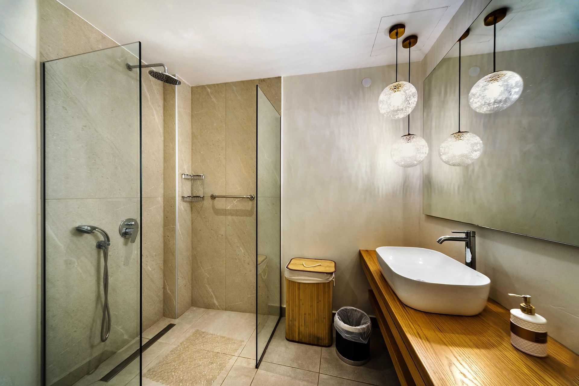Modern bathroom with a glass shower, wooden vanity, and decorative pendant lights.
