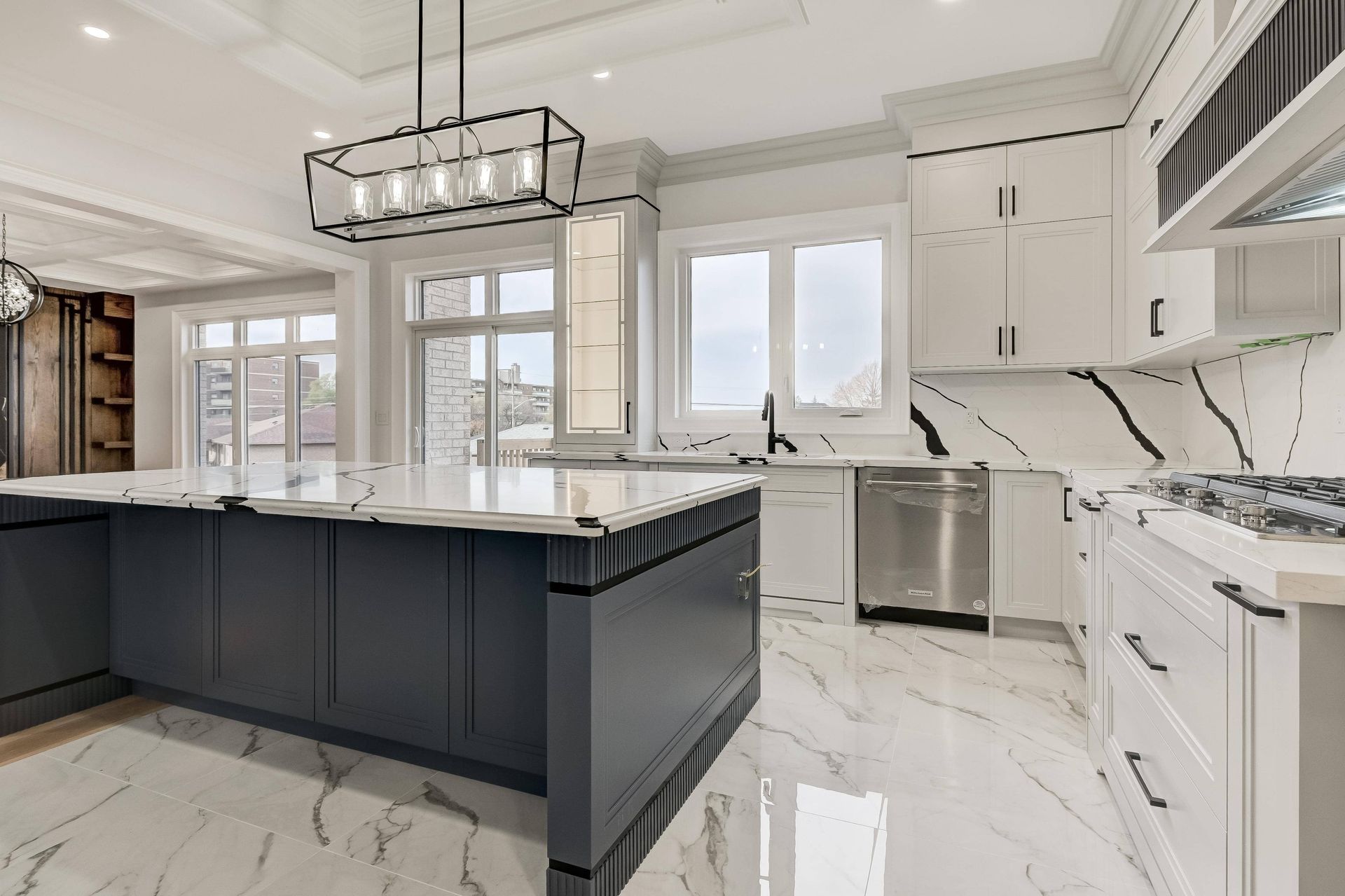 Modern kitchen with a large grey island, white cabinets, and marble countertops.