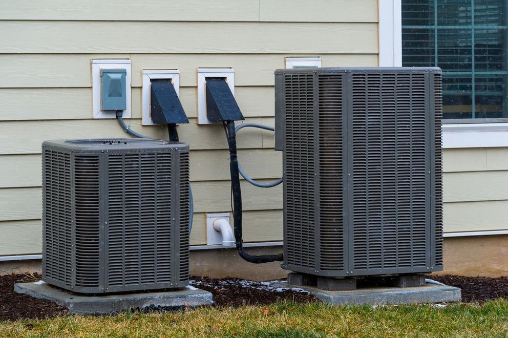 Two air conditioners are sitting outside of a house.