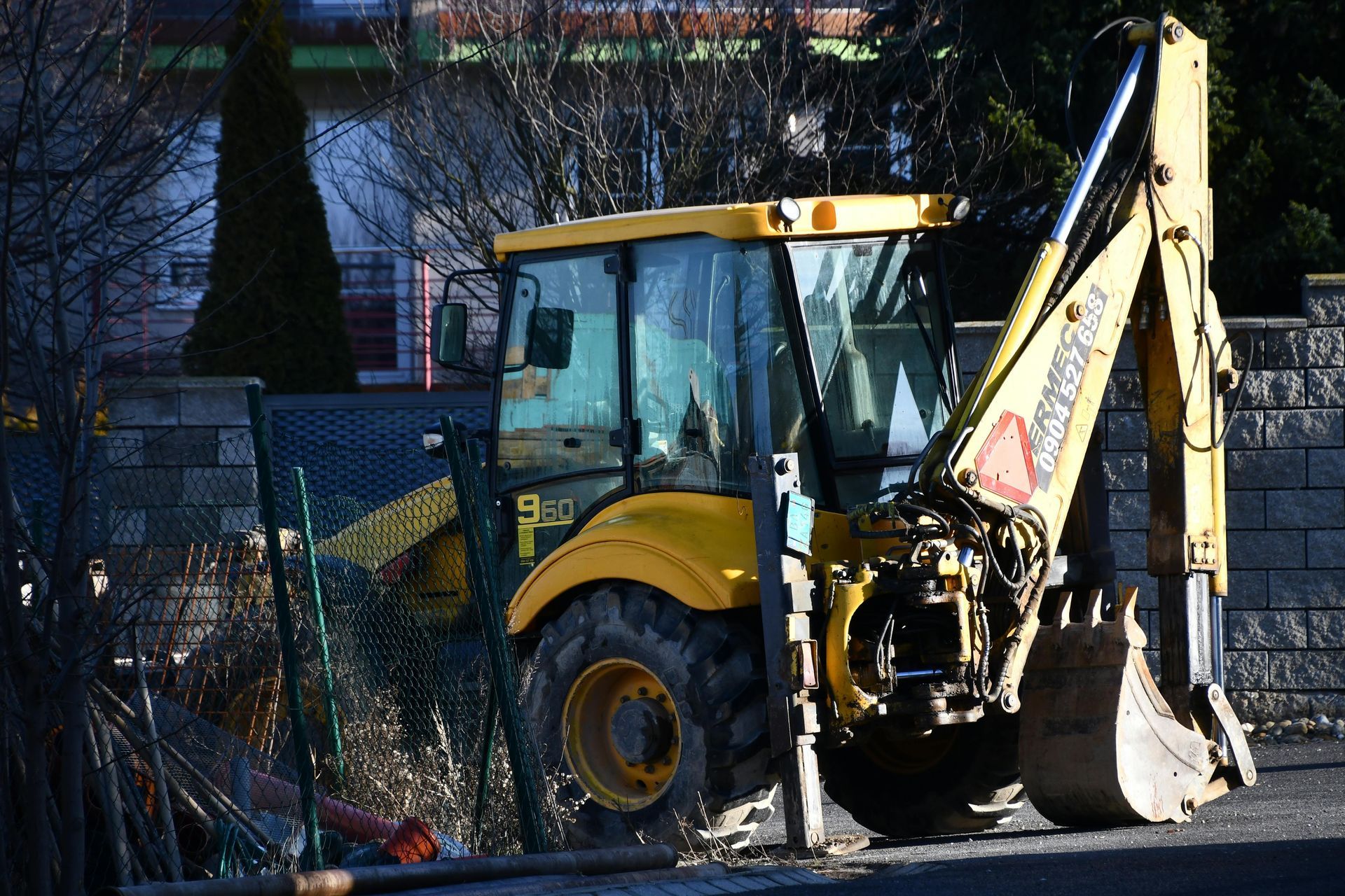 Yellow backhoe parked near a fence in a residential area.