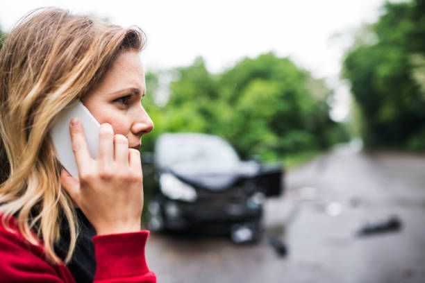 A close-up of a young woman on the phone standing by the damaged car after a car accident