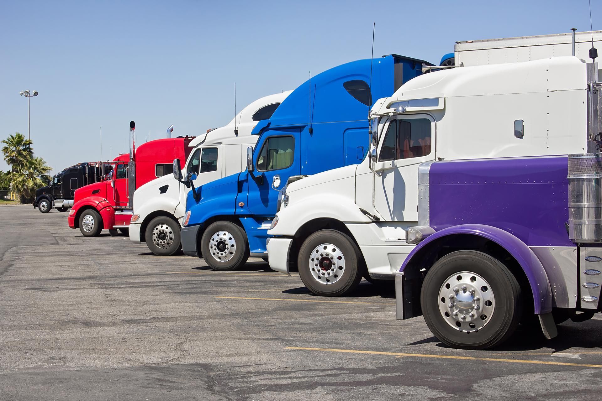 A row of semi trucks are parked in a parking lot.