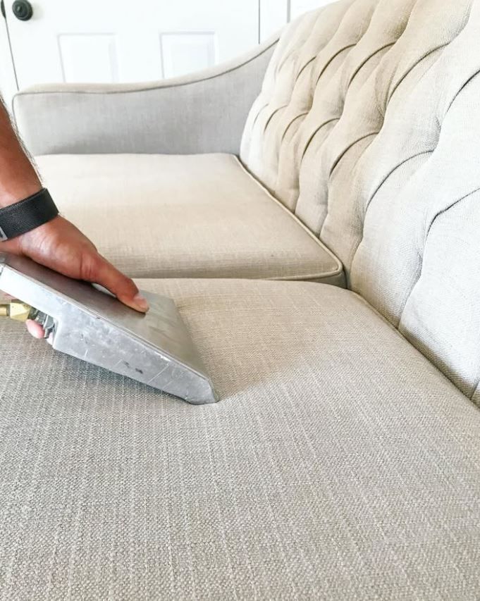 A person is cleaning a couch with a vacuum cleaner.