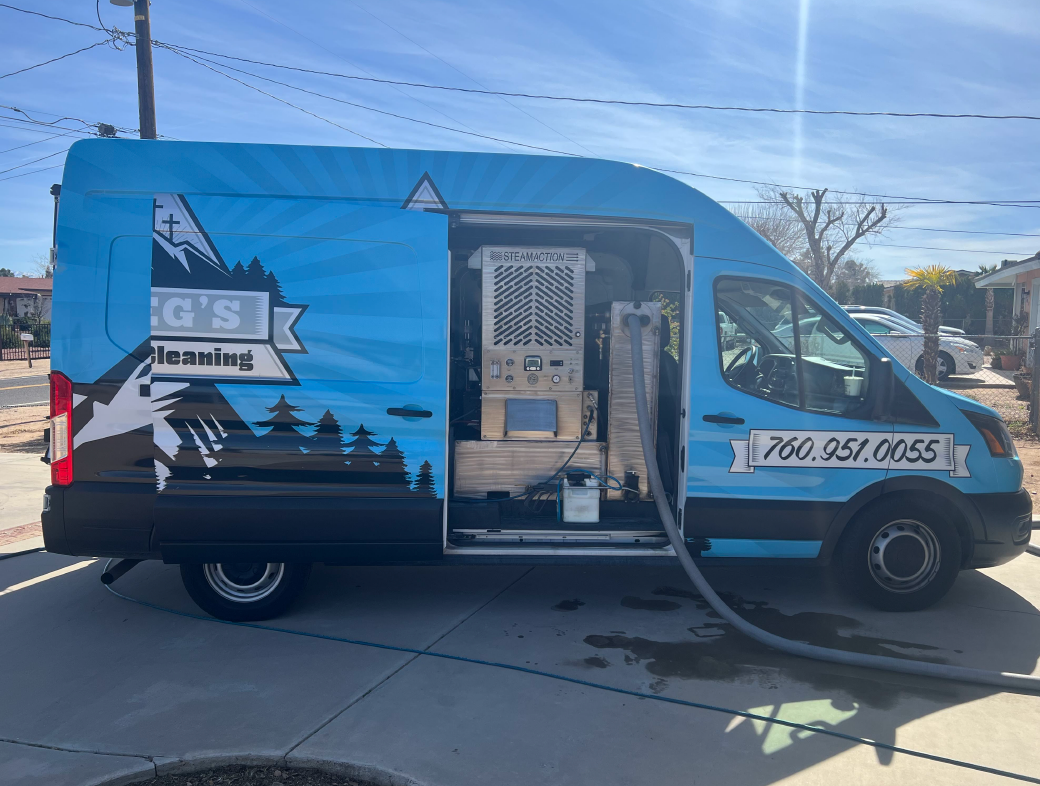 Blue service van with door open showing cleaning gear, mountain logo, and phone number, parked in a driveway.