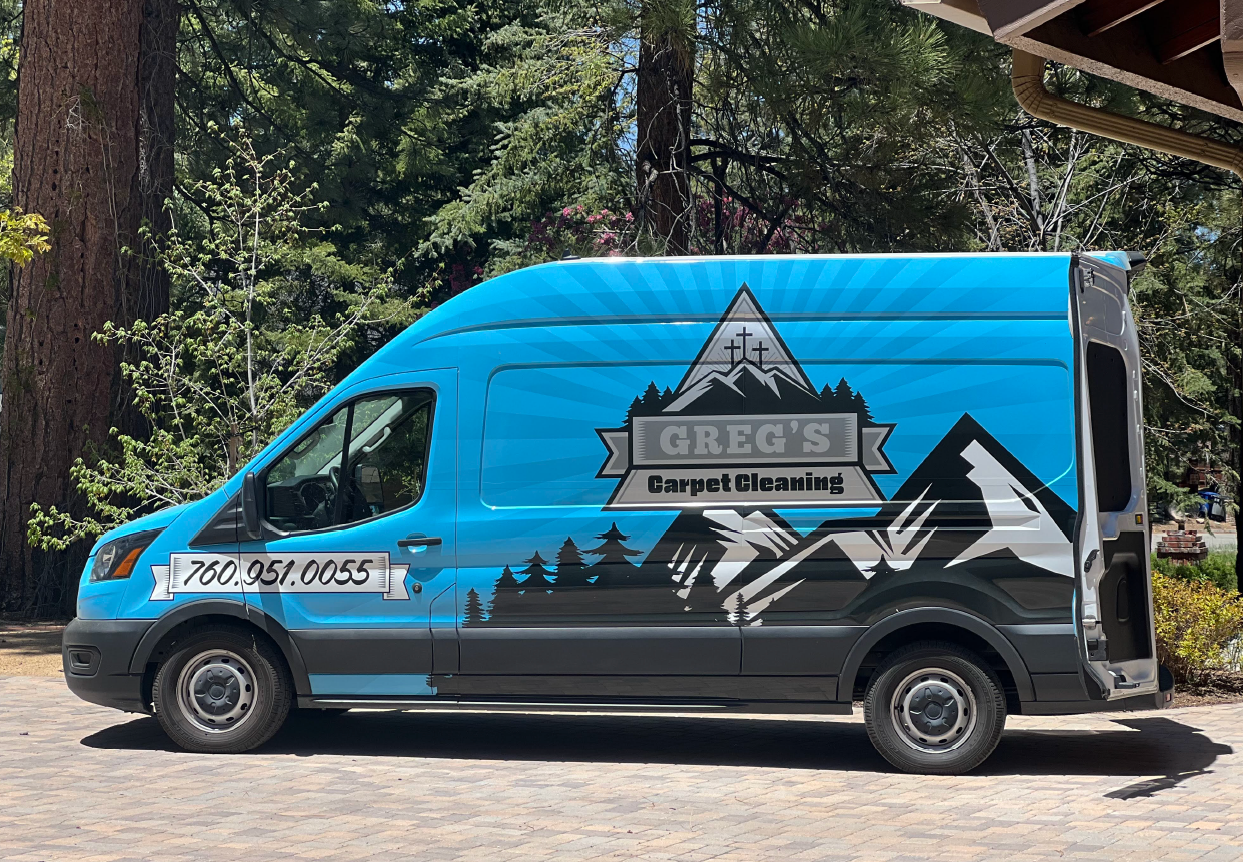 Blue service van with door open showing cleaning gear, mountain logo, and phone number, parked in a driveway.
