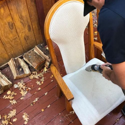 A man is cleaning a chair with a vacuum cleaner.