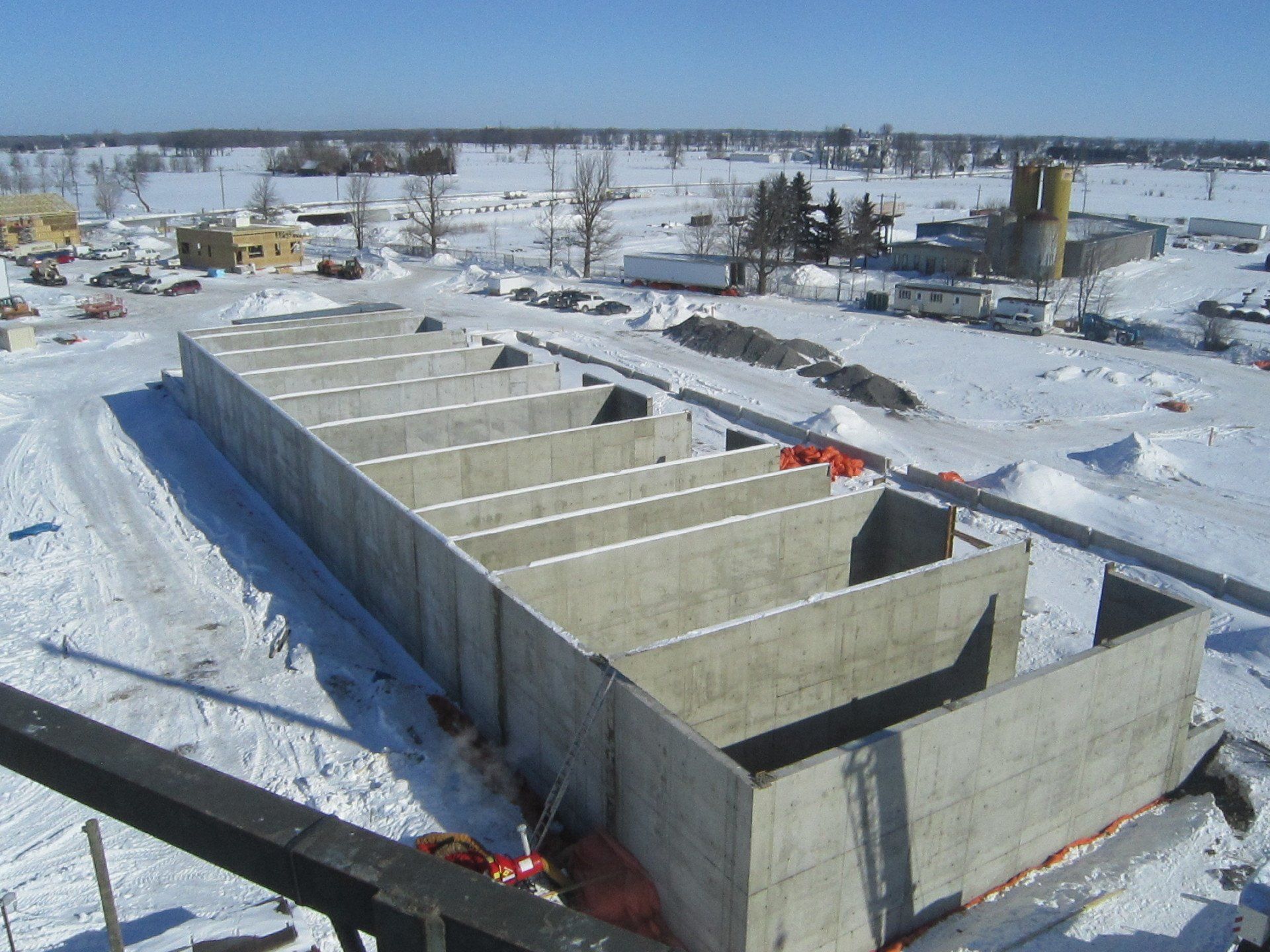 Concrete foundation with internal walls, under construction in a snow-covered field.