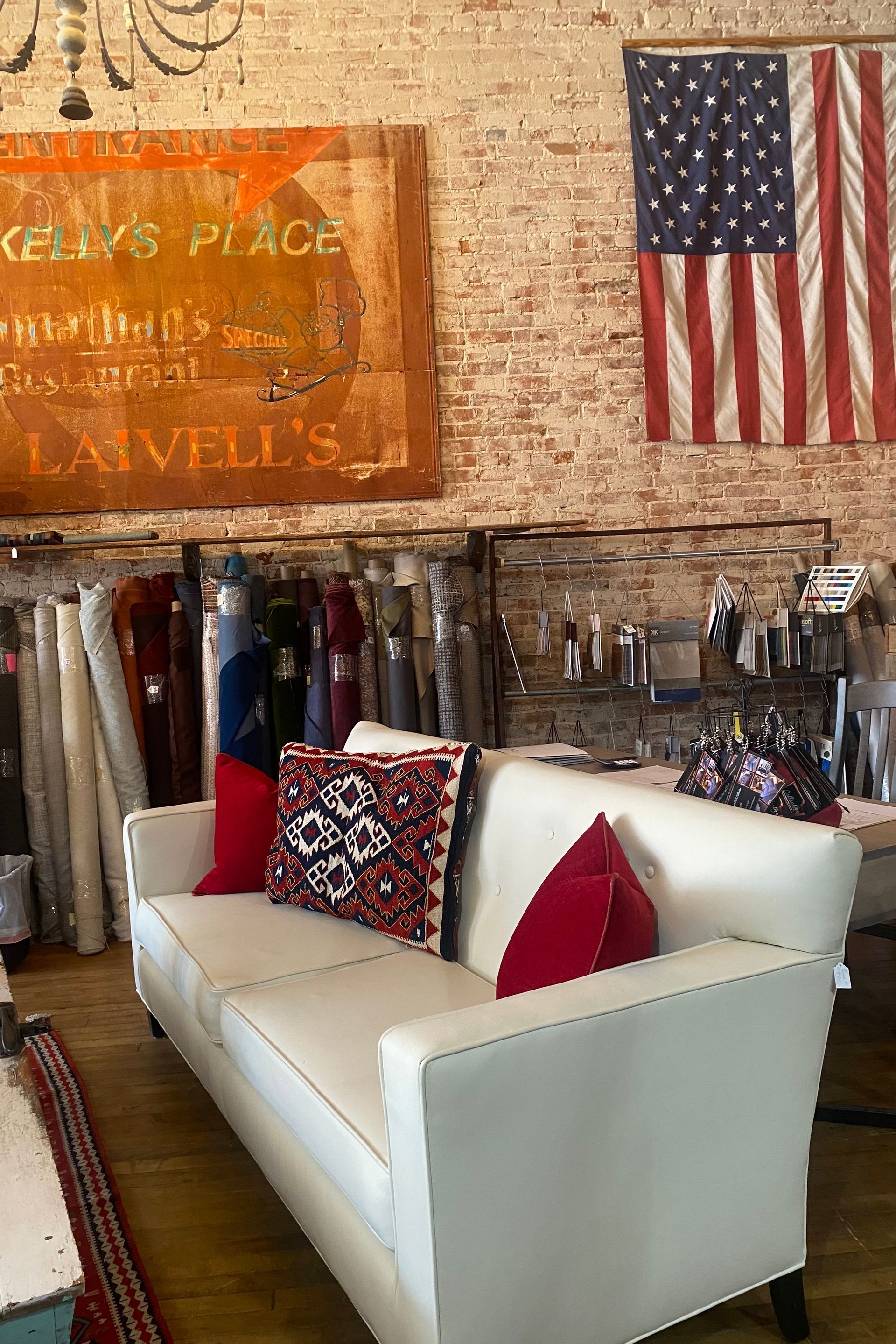 A white couch with red pillows is sitting in a room with an american flag hanging on the wall.