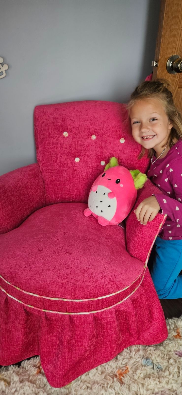 A little girl is sitting in a pink chair with a stuffed animal on it.