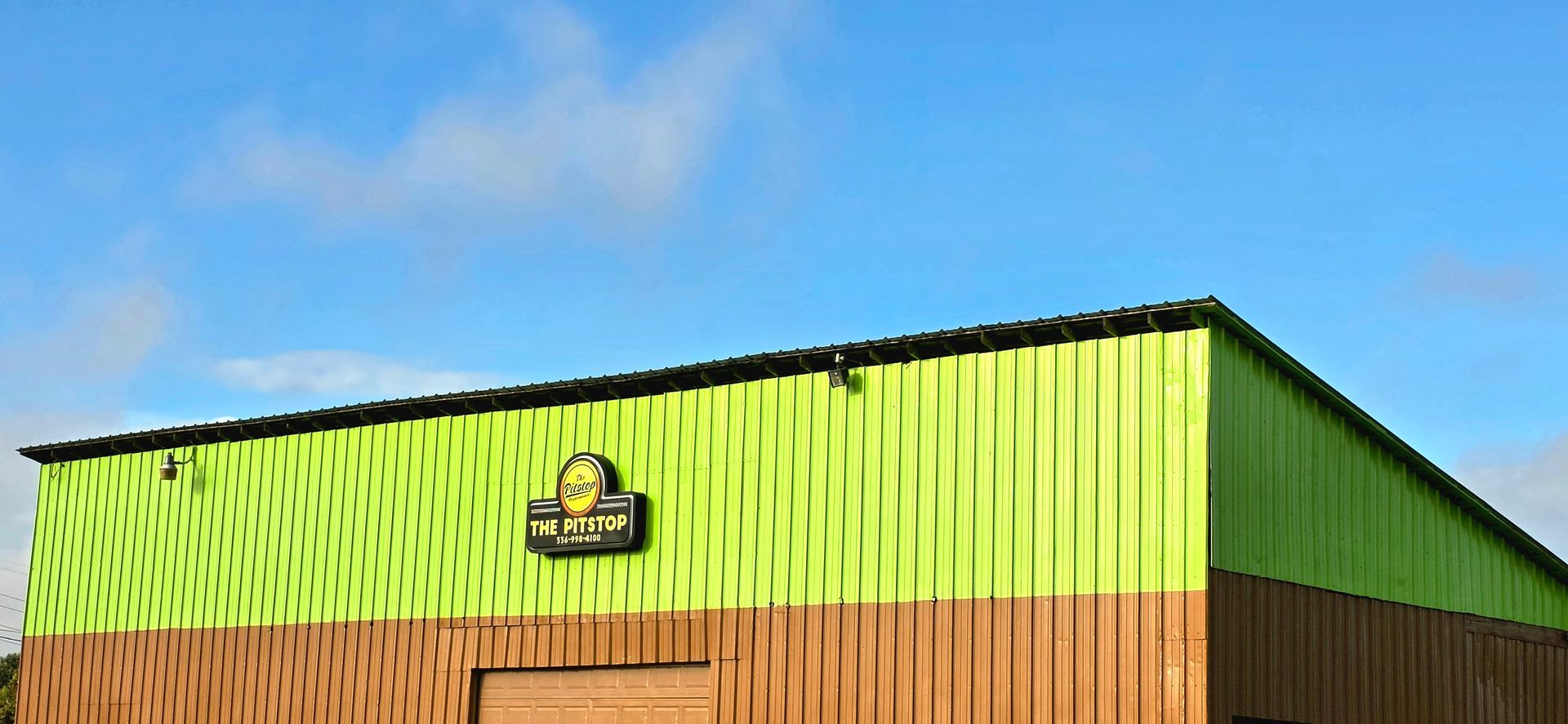 A building with green and brown walls against a blue sky with clouds.