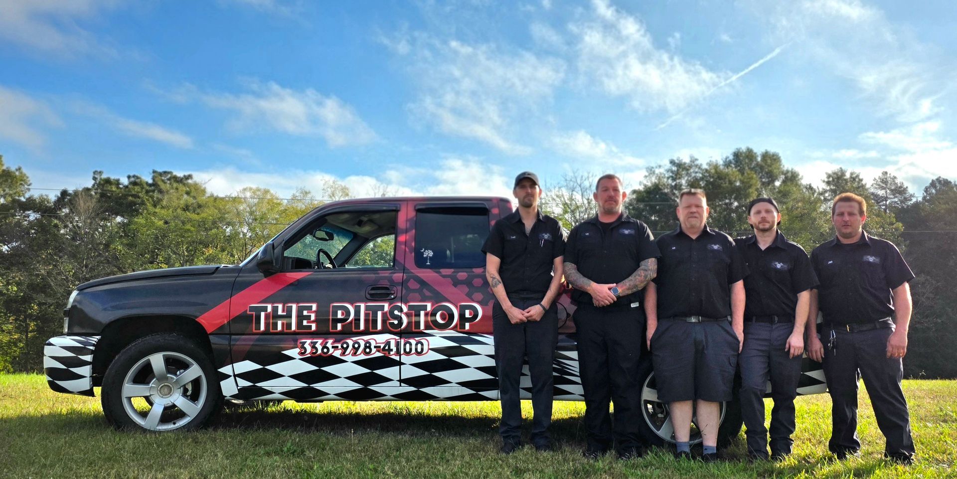 A team of six men in uniform stand in front of a truck with a company logo, on a grassy field.