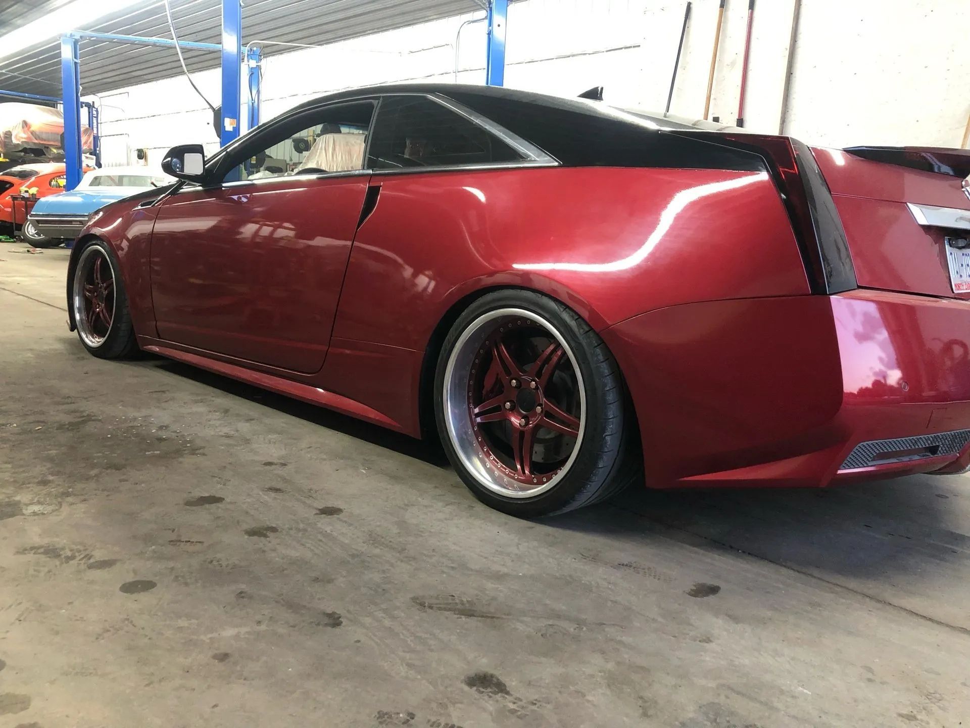 Red Cadillac coupe with custom red rims in a garage.