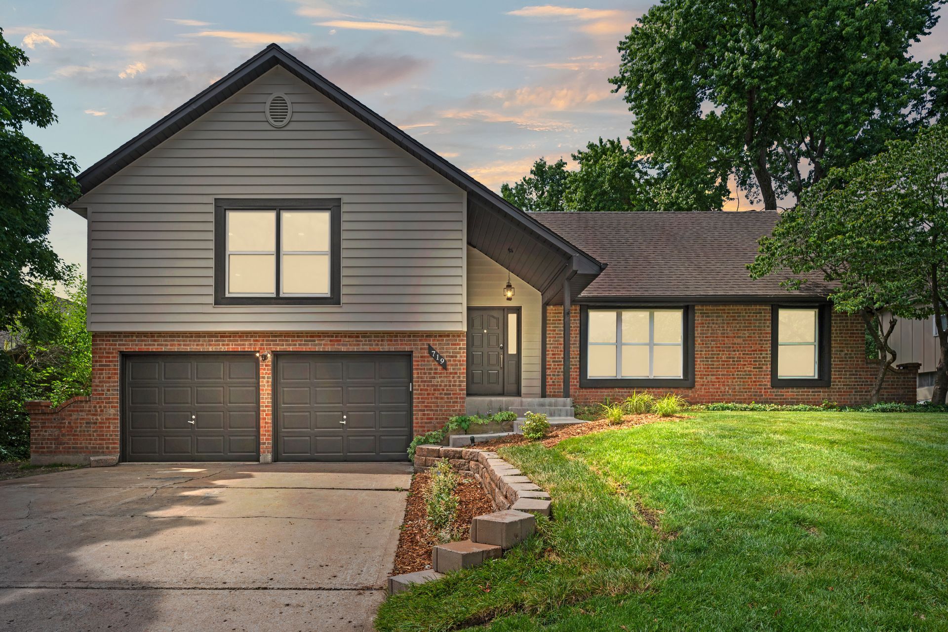 A large brick house with two garages and a large lawn in front of it.