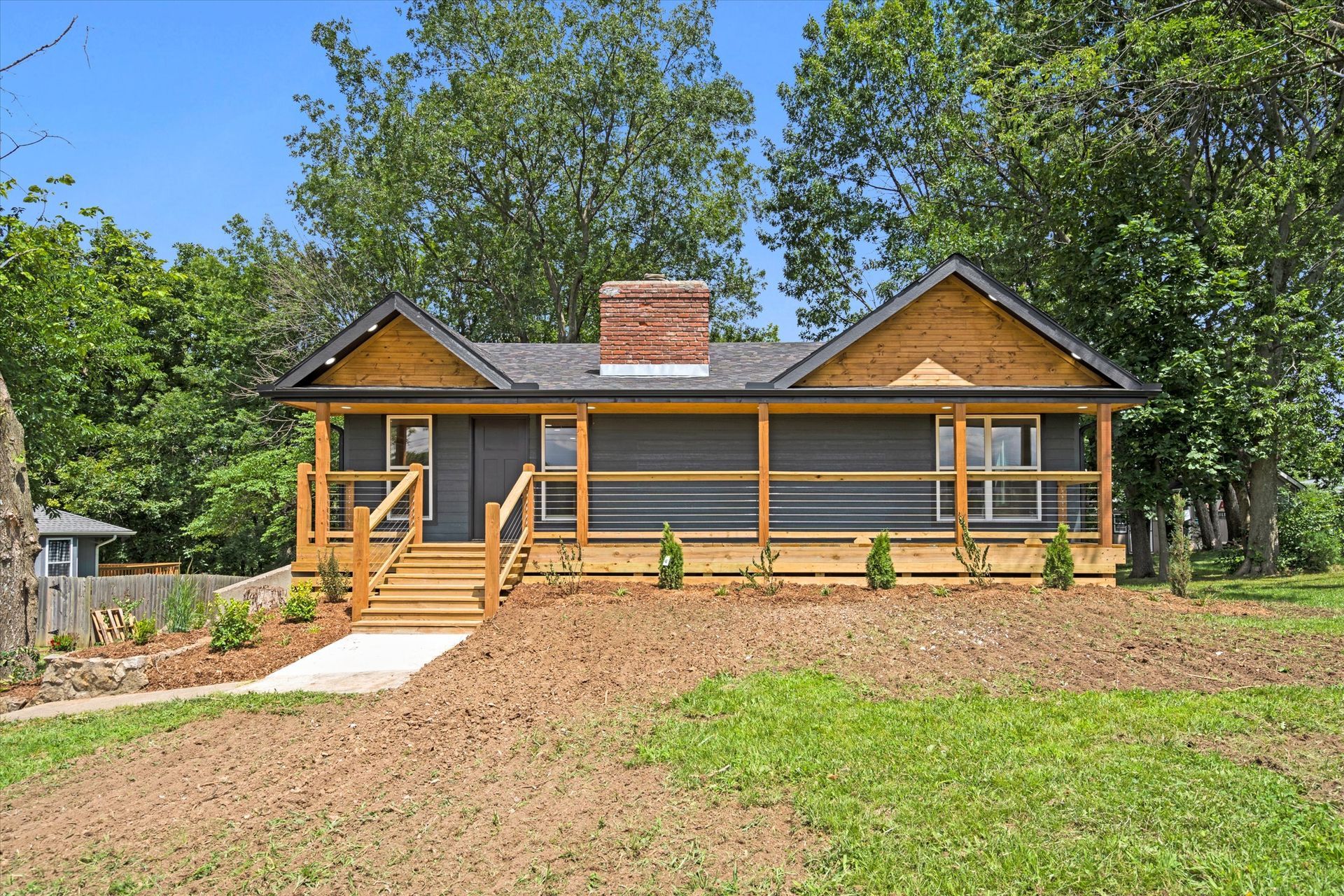 A small house with a porch and stairs is sitting on top of a grassy hill.