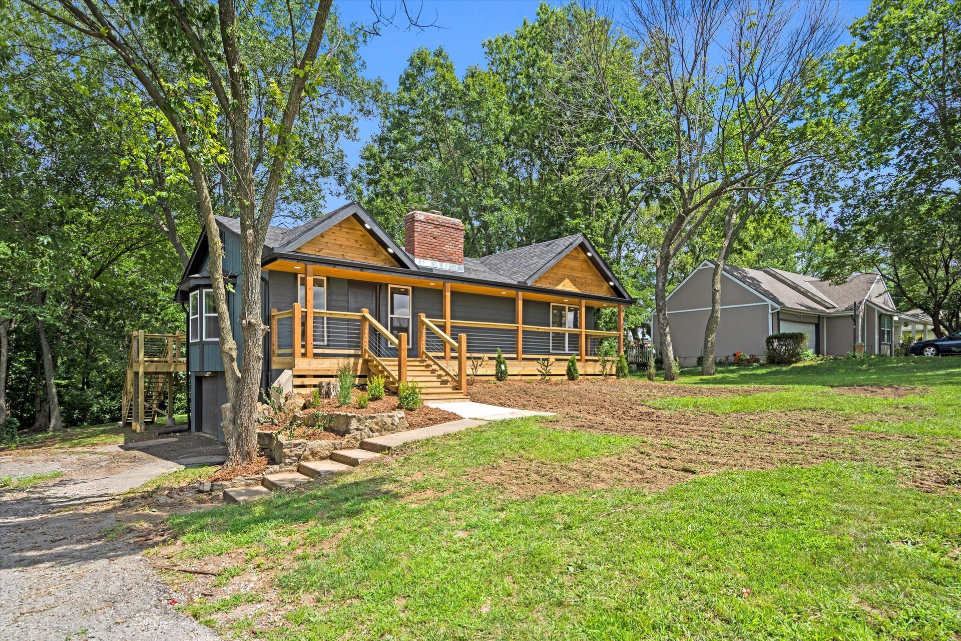 A house with a porch is sitting on top of a lush green lawn surrounded by trees.
