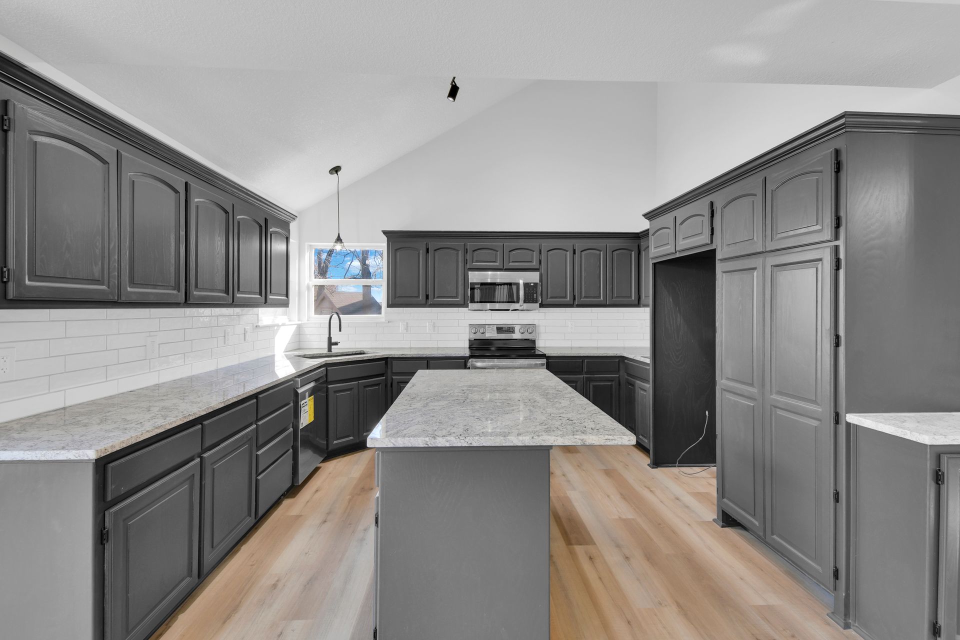 A kitchen with gray cabinets , granite counter tops , and a large island.