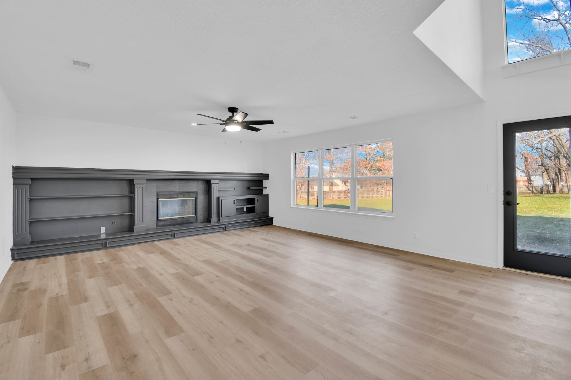An empty living room with hardwood floors , a fireplace and a ceiling fan.