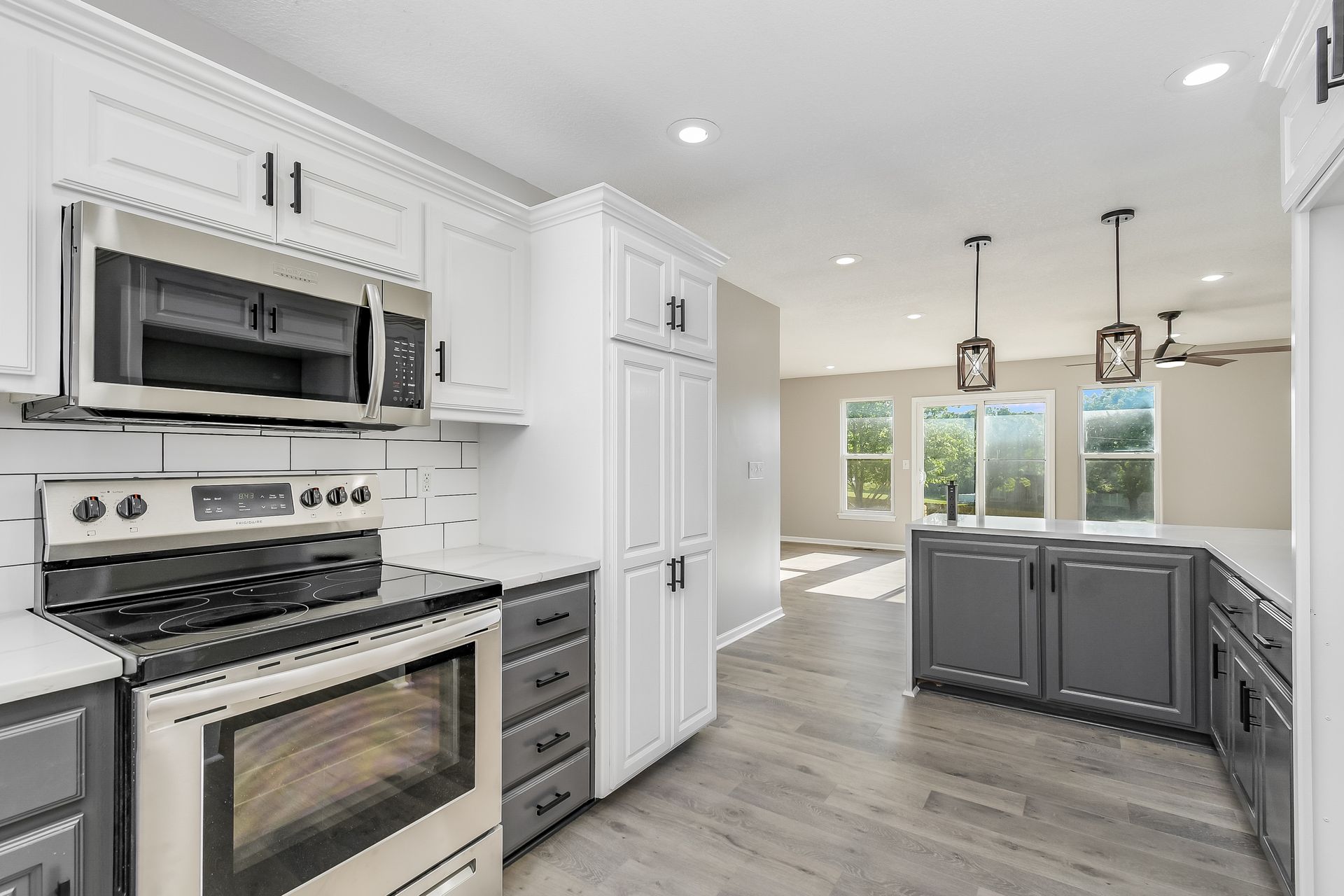A kitchen with white cabinets , a stove , a microwave , and a refrigerator.