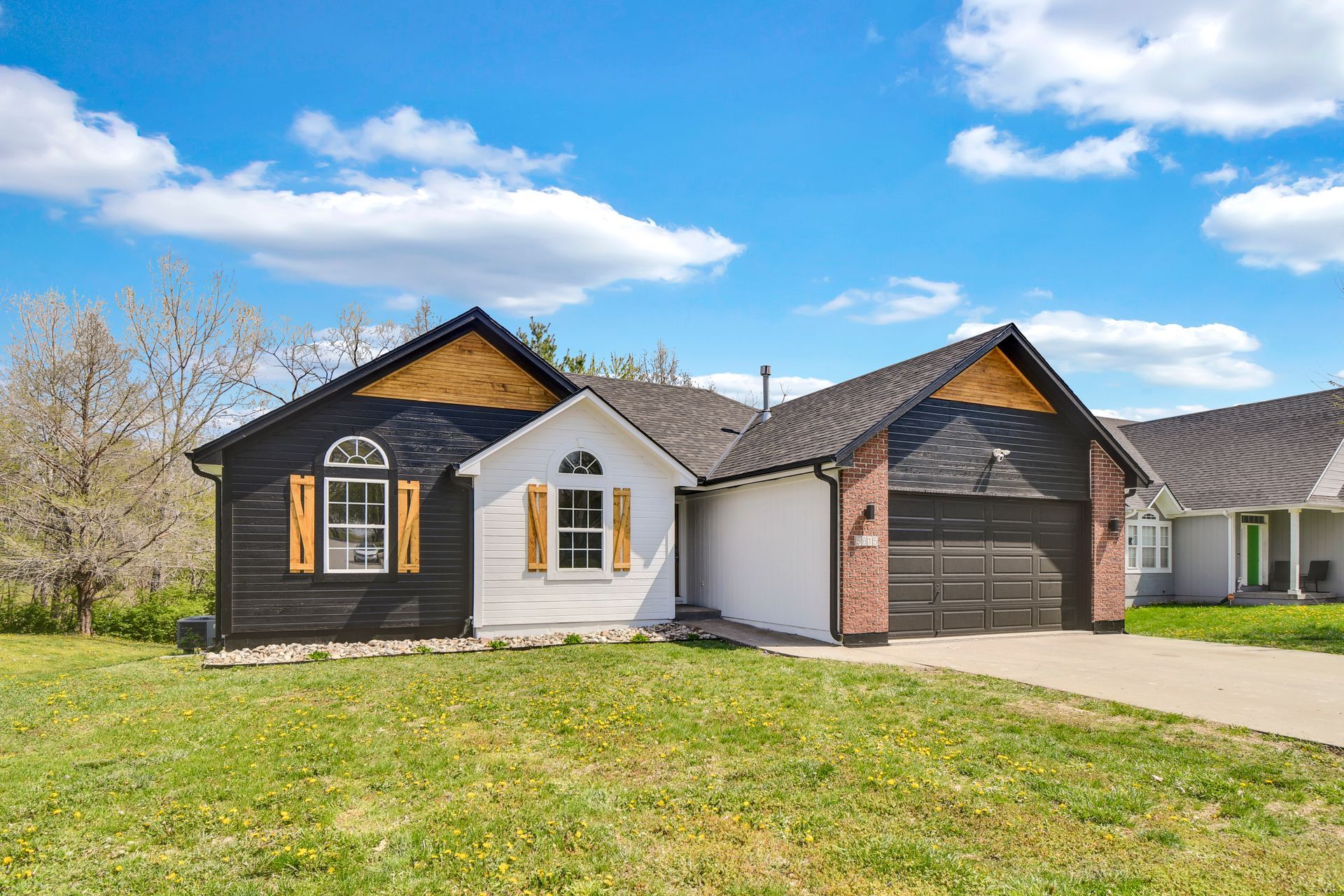 A white house with a black roof and natural wood shutters is sitting on top of a lush green lawn.