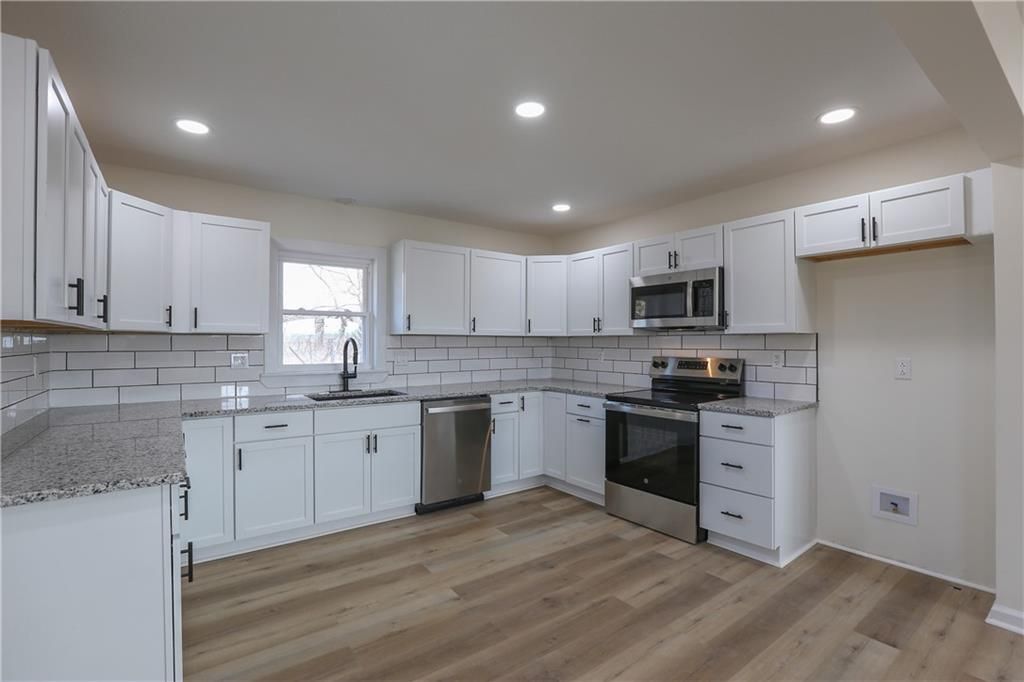 A kitchen with white cabinets , granite counter tops , stainless steel appliances and hardwood floors.