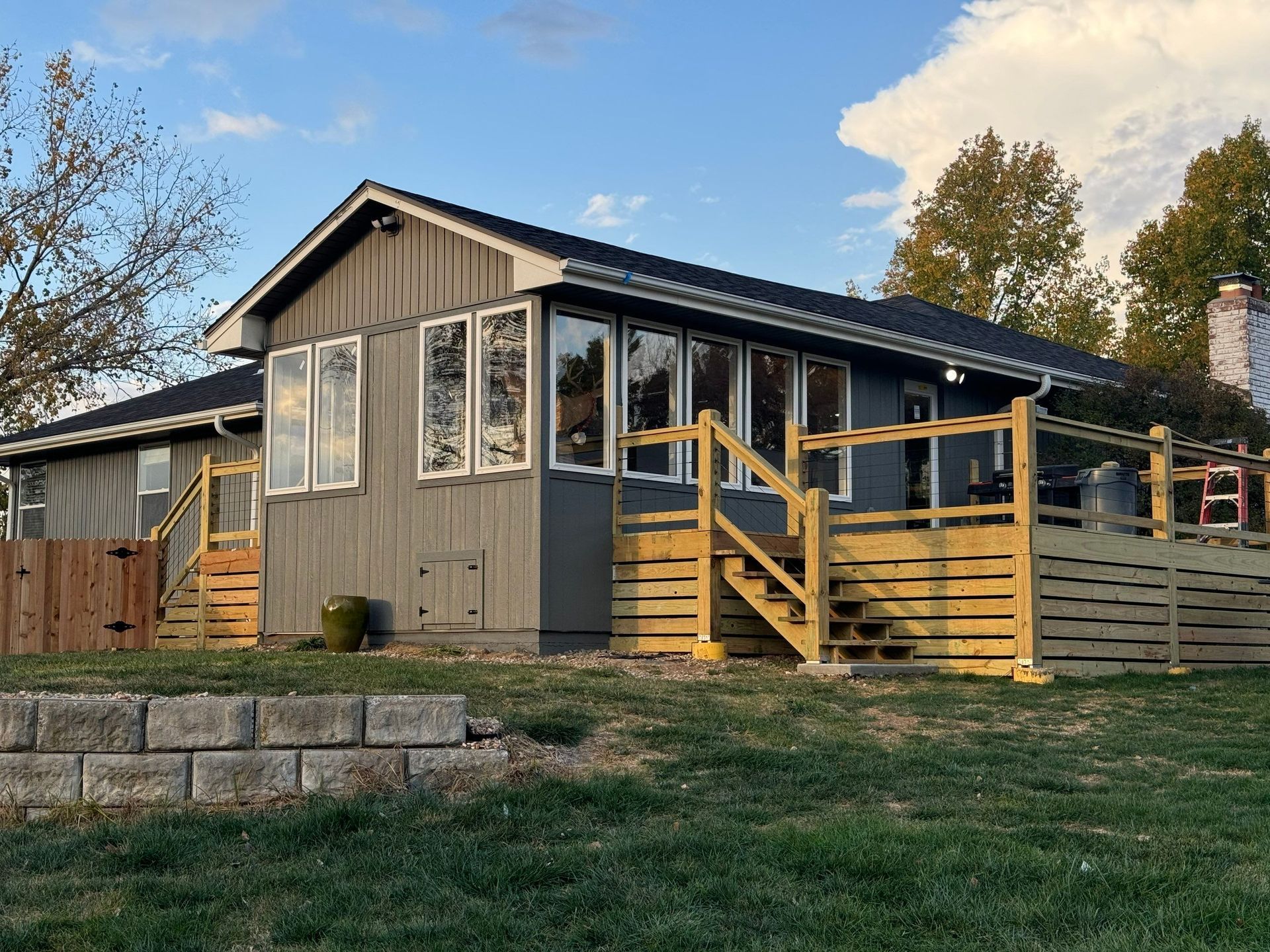A house with a wooden deck and stairs is sitting on top of a lush green lawn.