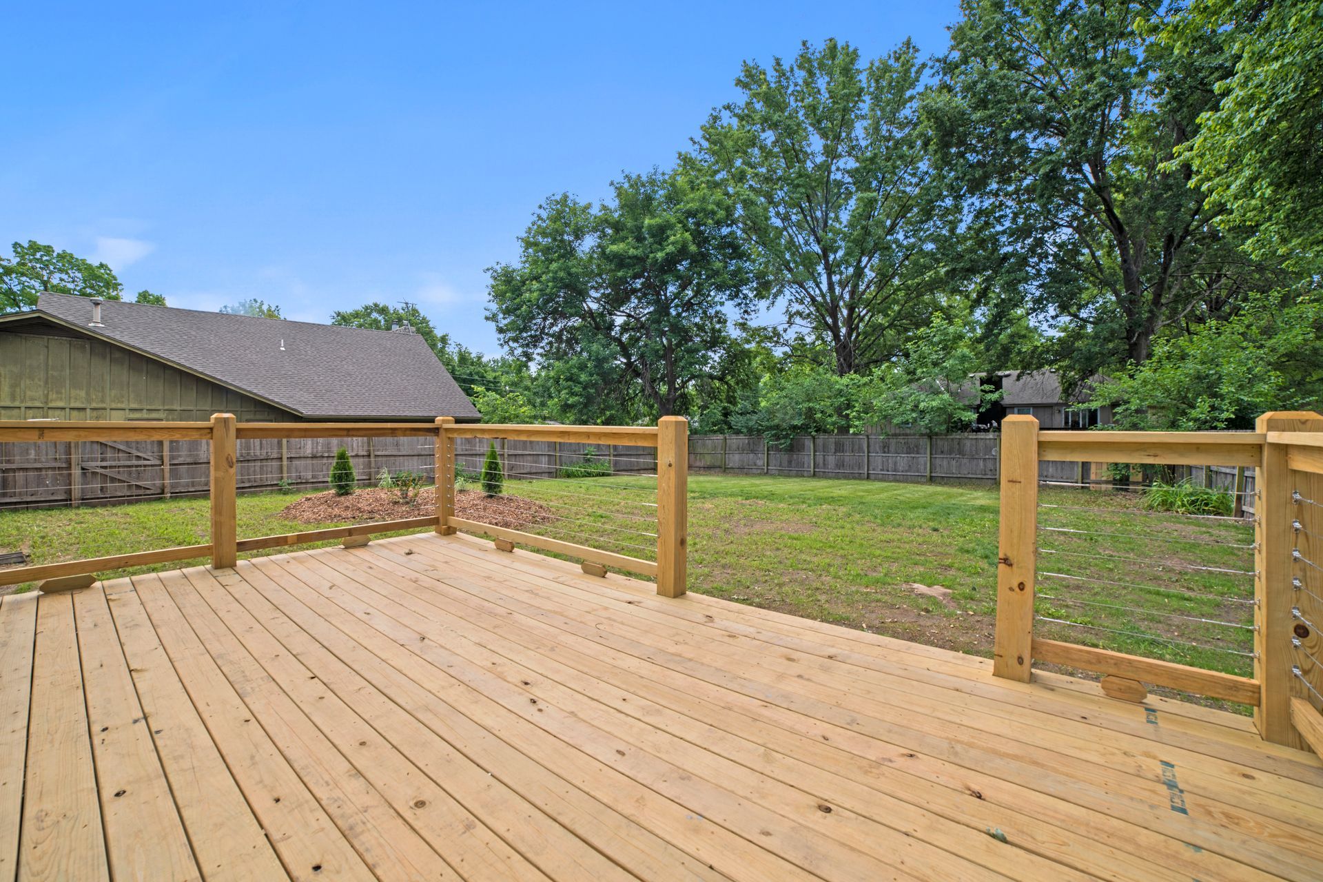An empty wooden deck with a wooden fence and a house in the background.