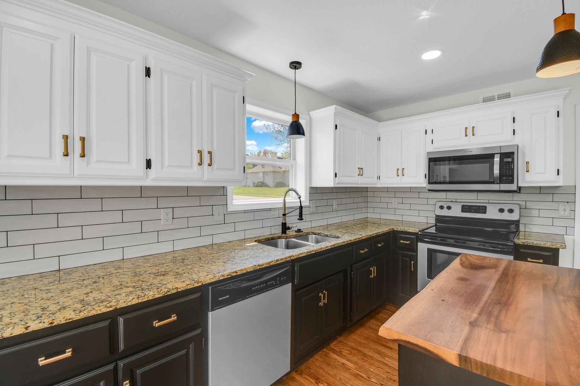 A kitchen with black cabinets , granite counter tops , stainless steel appliances and a wooden island.