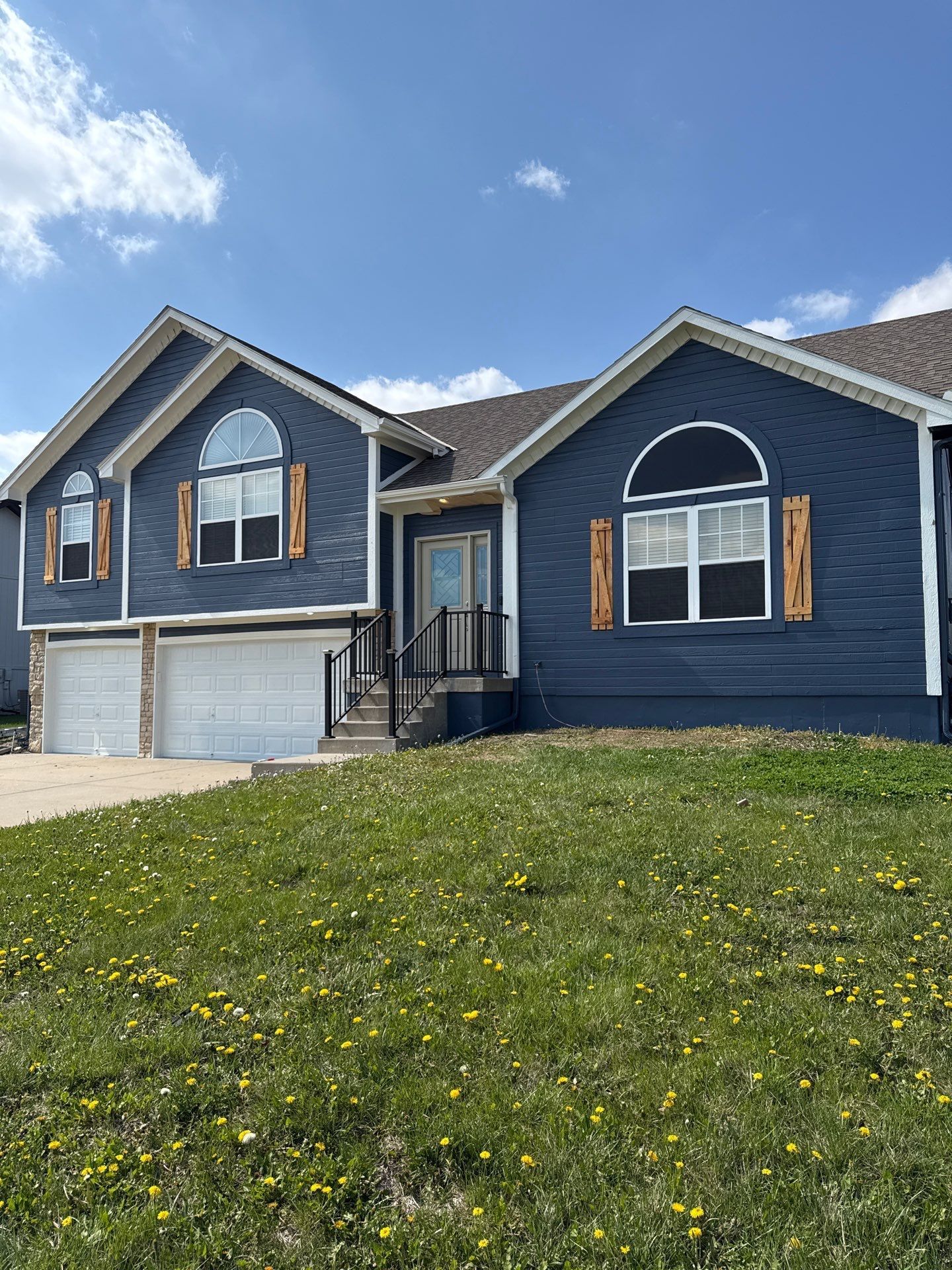 A large blue house with two garages is sitting on top of a grassy lawn.