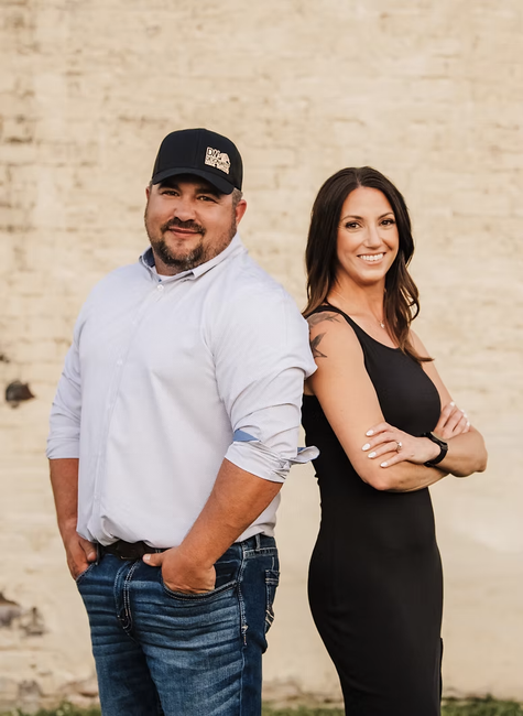 Devon and Andrea West are standing back to back in front of a brick wall.