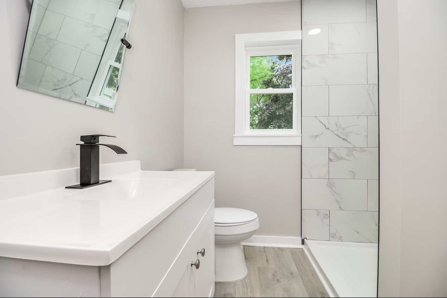 A bathroom with a toilet , sink , mirror and walk in shower.