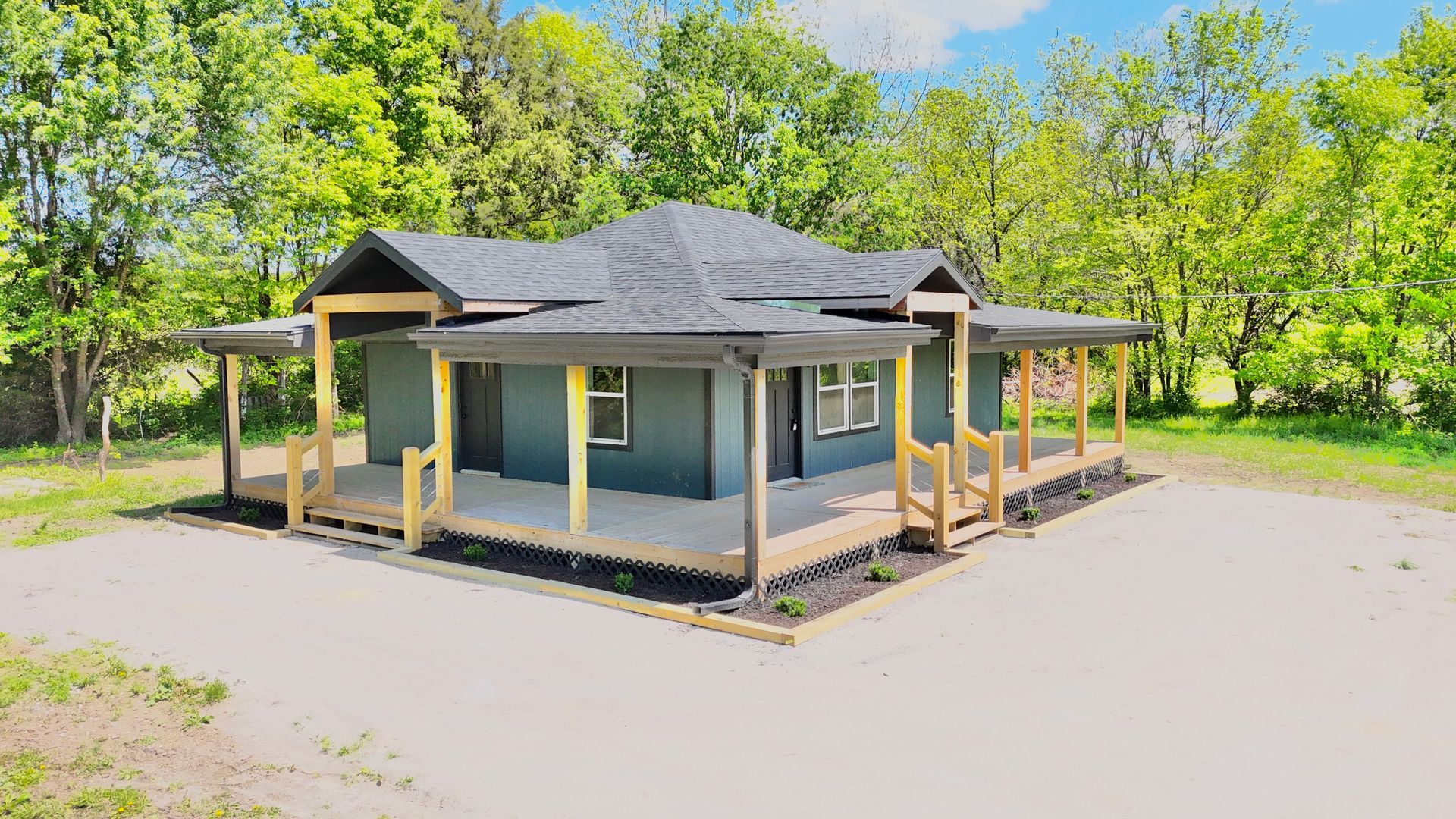 A small house with a wraparound porch and trees in the background.