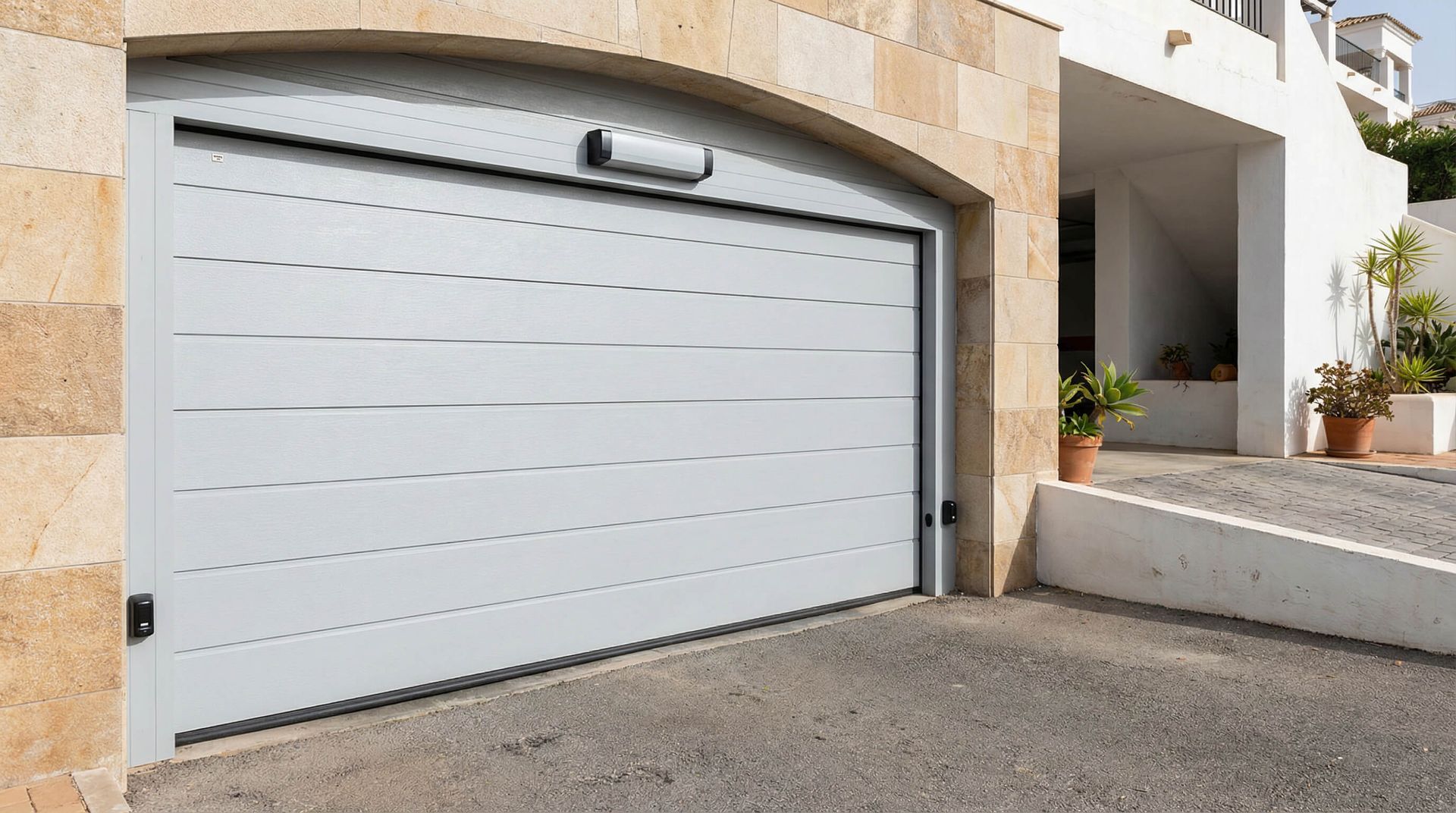 Puerta de garaje gris en una abertura arqueada de una casa de piedra beige.