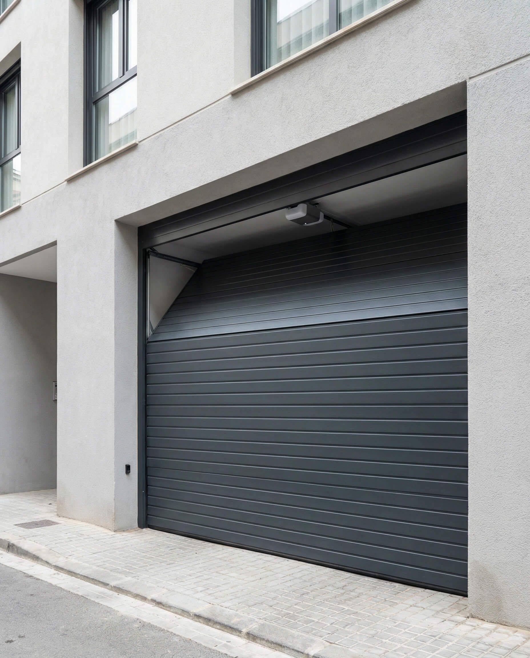 Puerta de garaje gris parcialmente abierta en la fachada de un edificio.