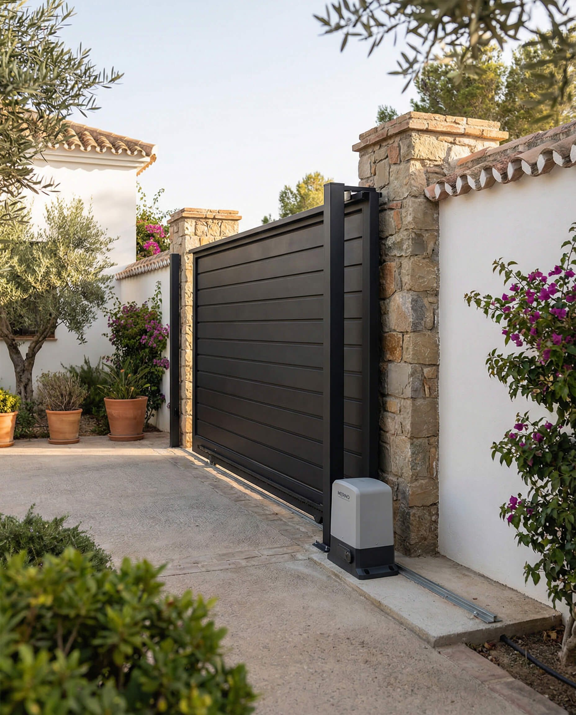 Puerta corrediza negra en pared de piedra y blanca, entrada a un camino de entrada.