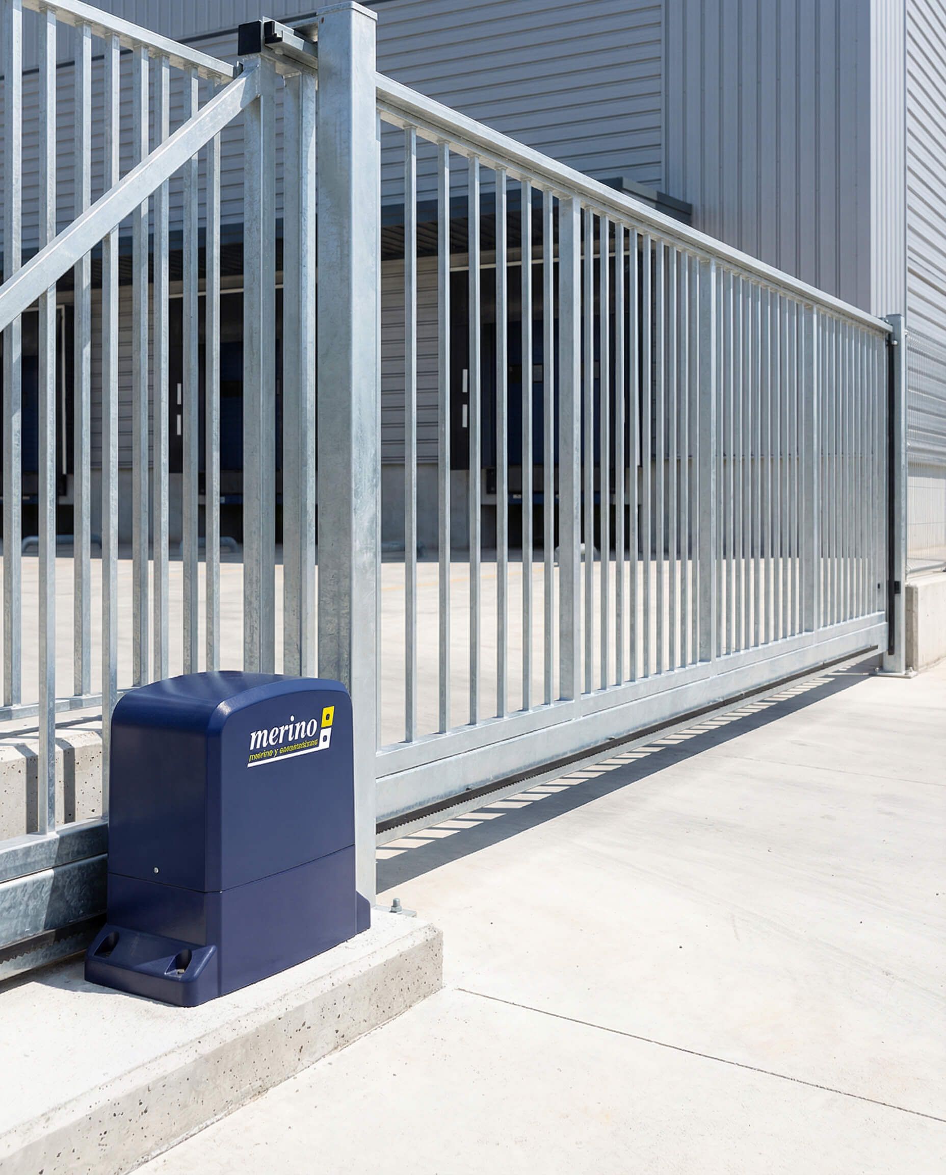 Puerta metálica corredera con sistema de apertura automatizado frente a un edificio.