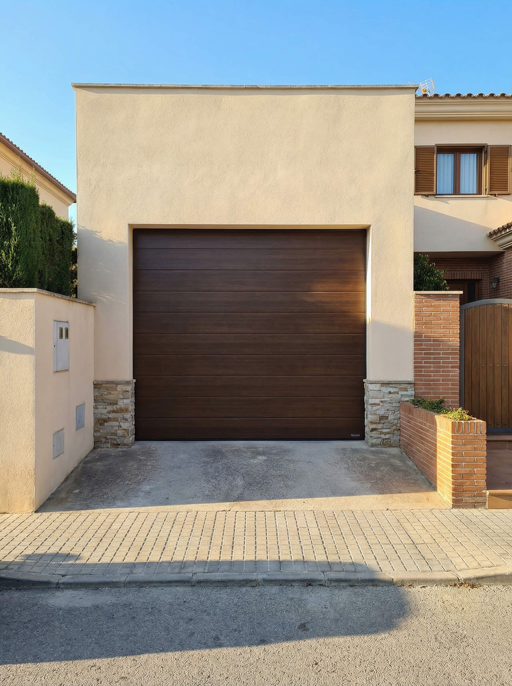 Puerta de garaje marrón en un edificio beige con entrada de ladrillo.