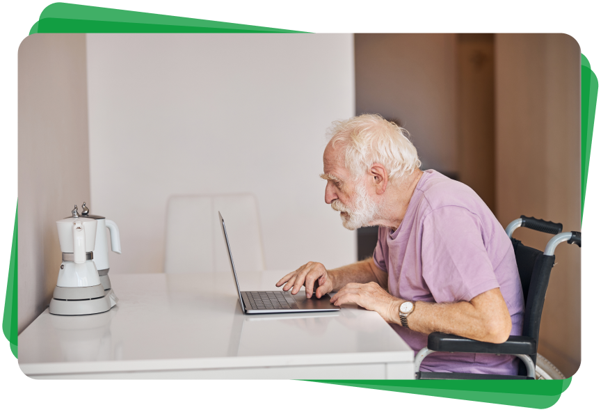 An elderly man in a wheelchair is using a laptop computer.