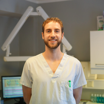 Helsearbeider i lyse skrubber står på en klinikk og smiler foran tannlegeutstyr.