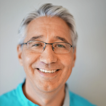 Smilende mann med briller og turkis skjorte mot en lys bakgrunn