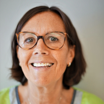 Smilende person med briller og neongrønn skjorte som ser inn i kameraet.