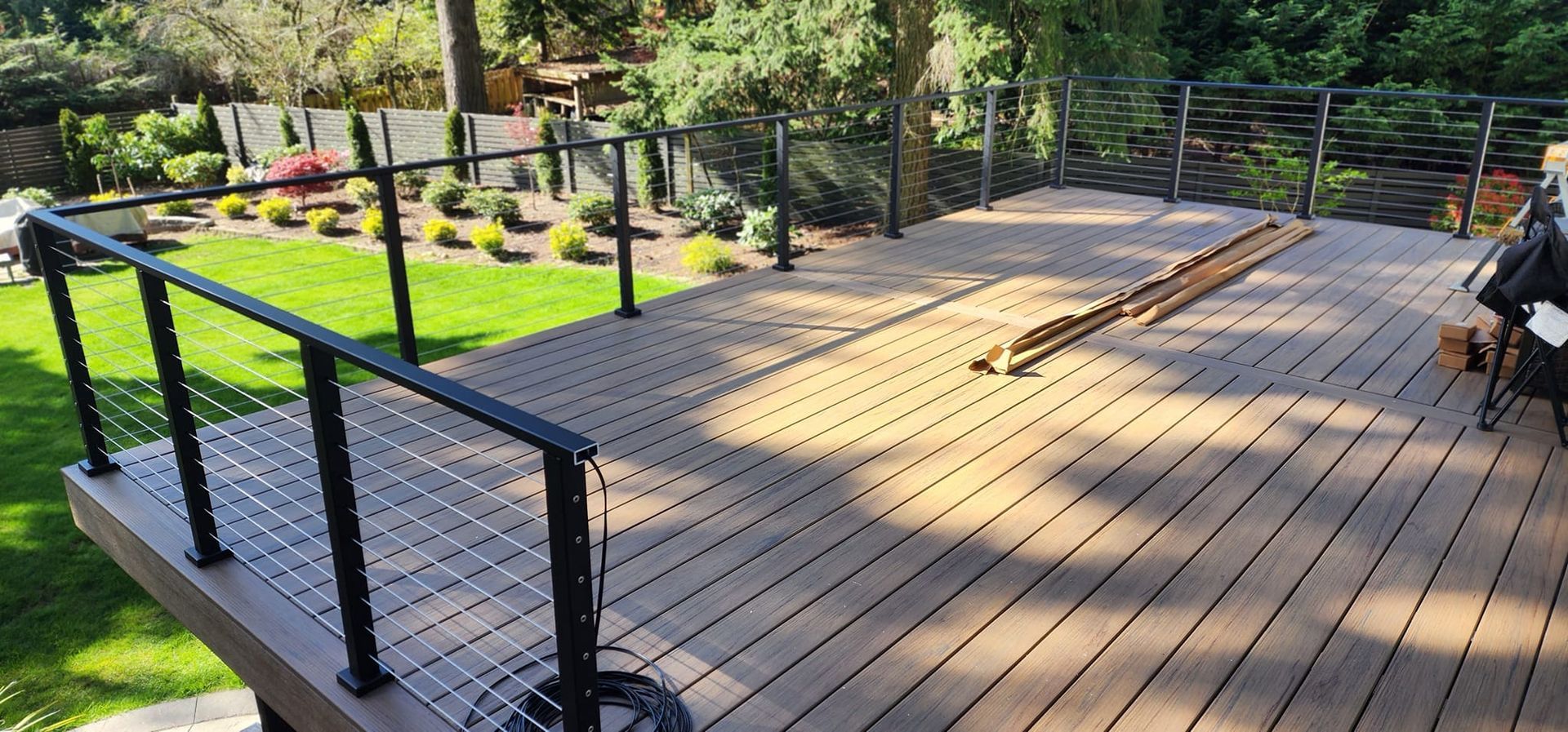 A wooden deck with a black railing in a backyard.