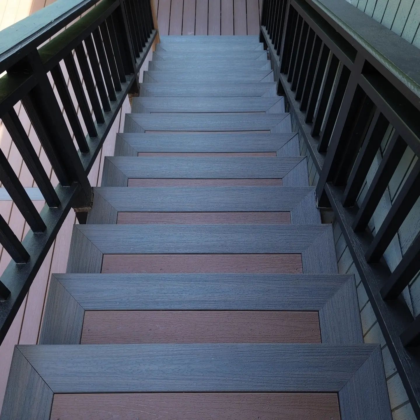 A wooden deck with stairs leading up to it is in the backyard of a house.