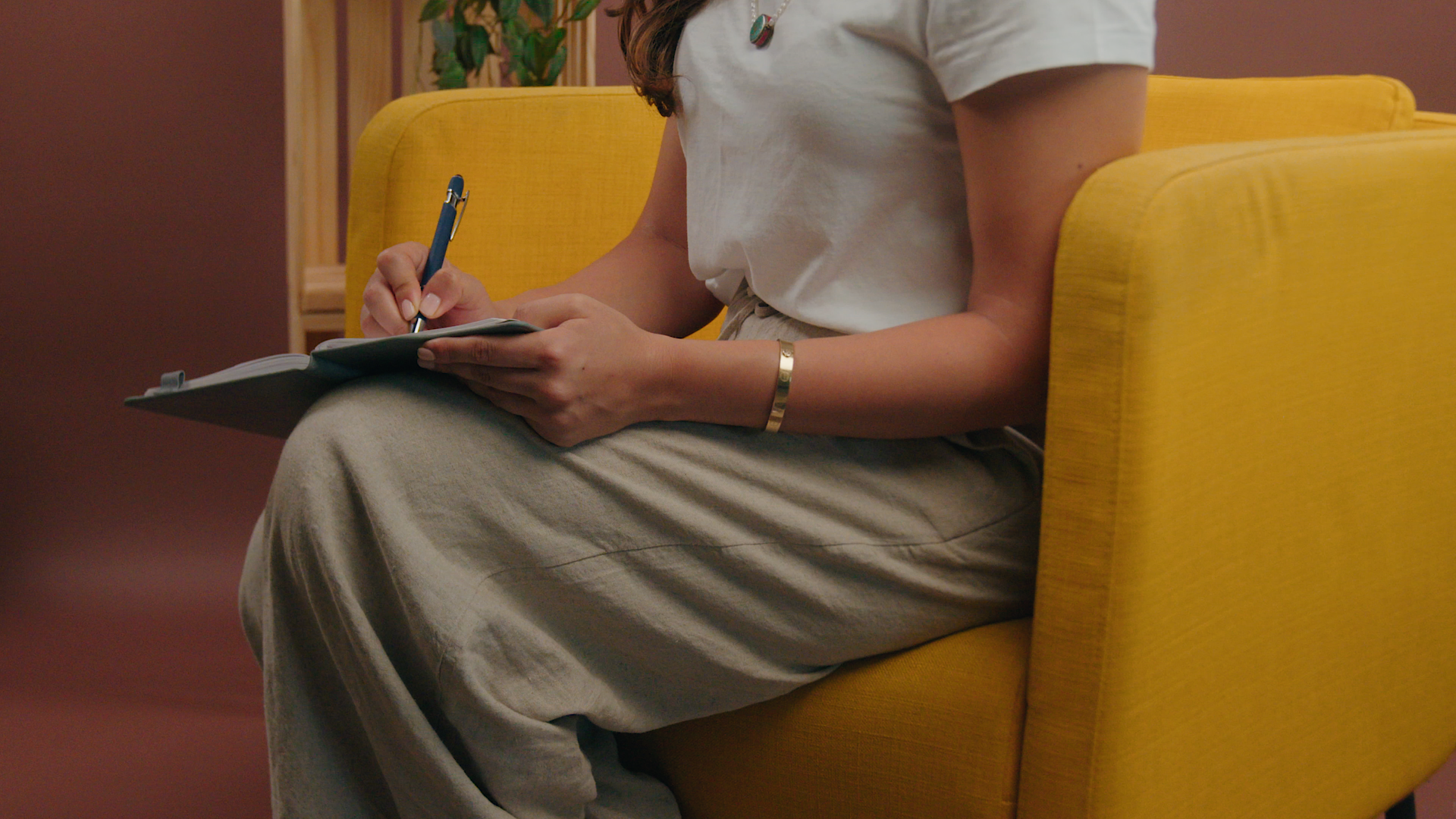 A woman is sitting in a yellow chair writing on a clipboard.
