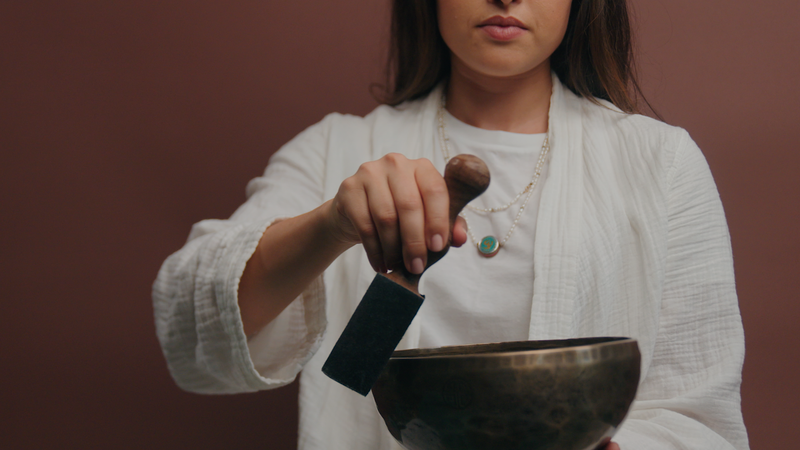 A woman is holding a bowl and a mallet in her hands.