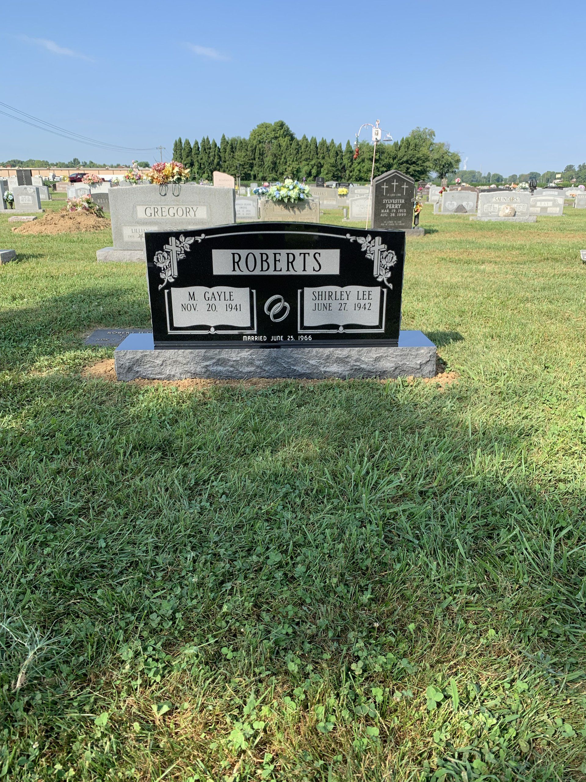 A black gravestone in a cemetery with a blue sky in the background.
