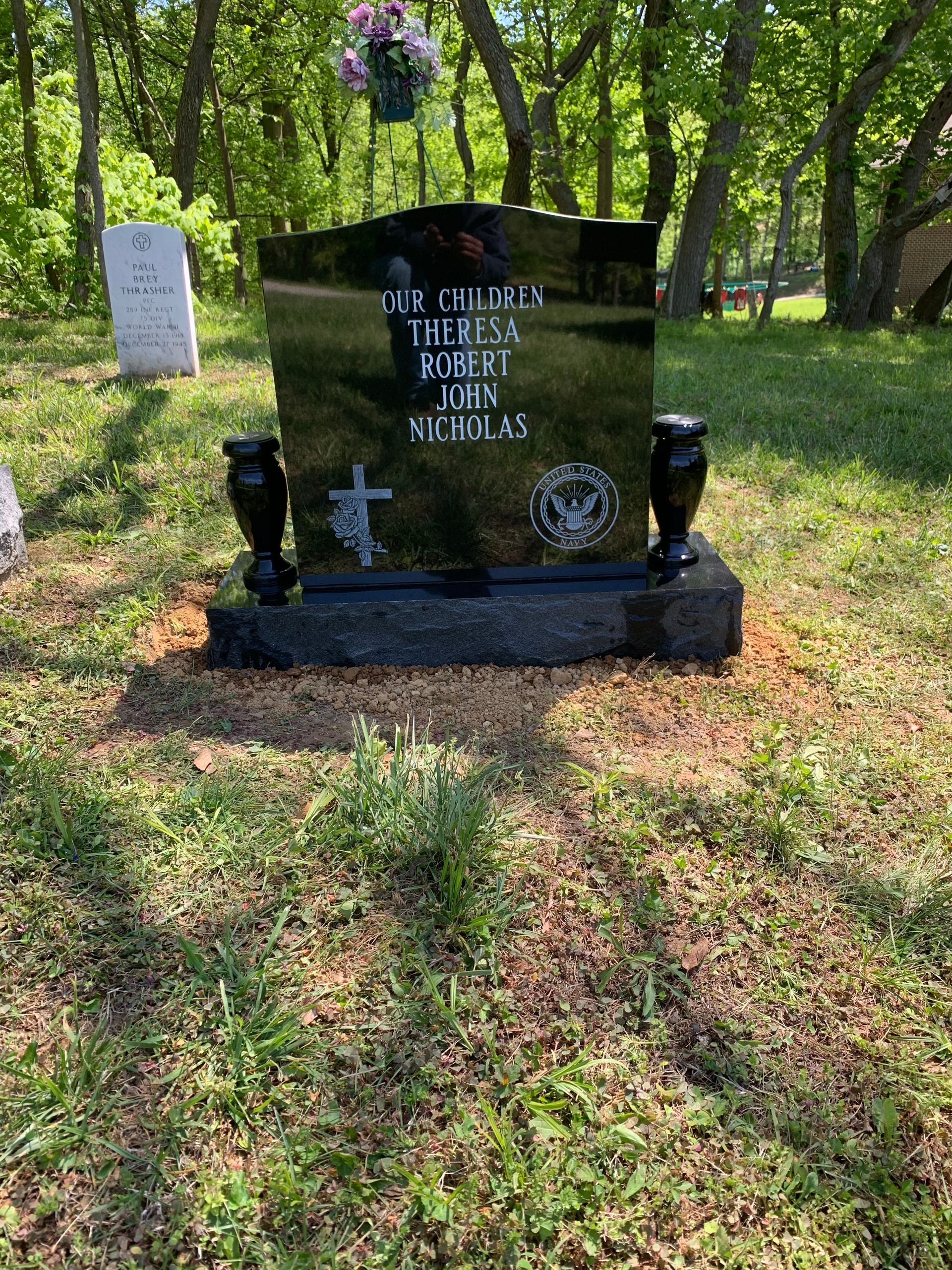 A black gravestone is sitting in the middle of a grassy field in a cemetery.
