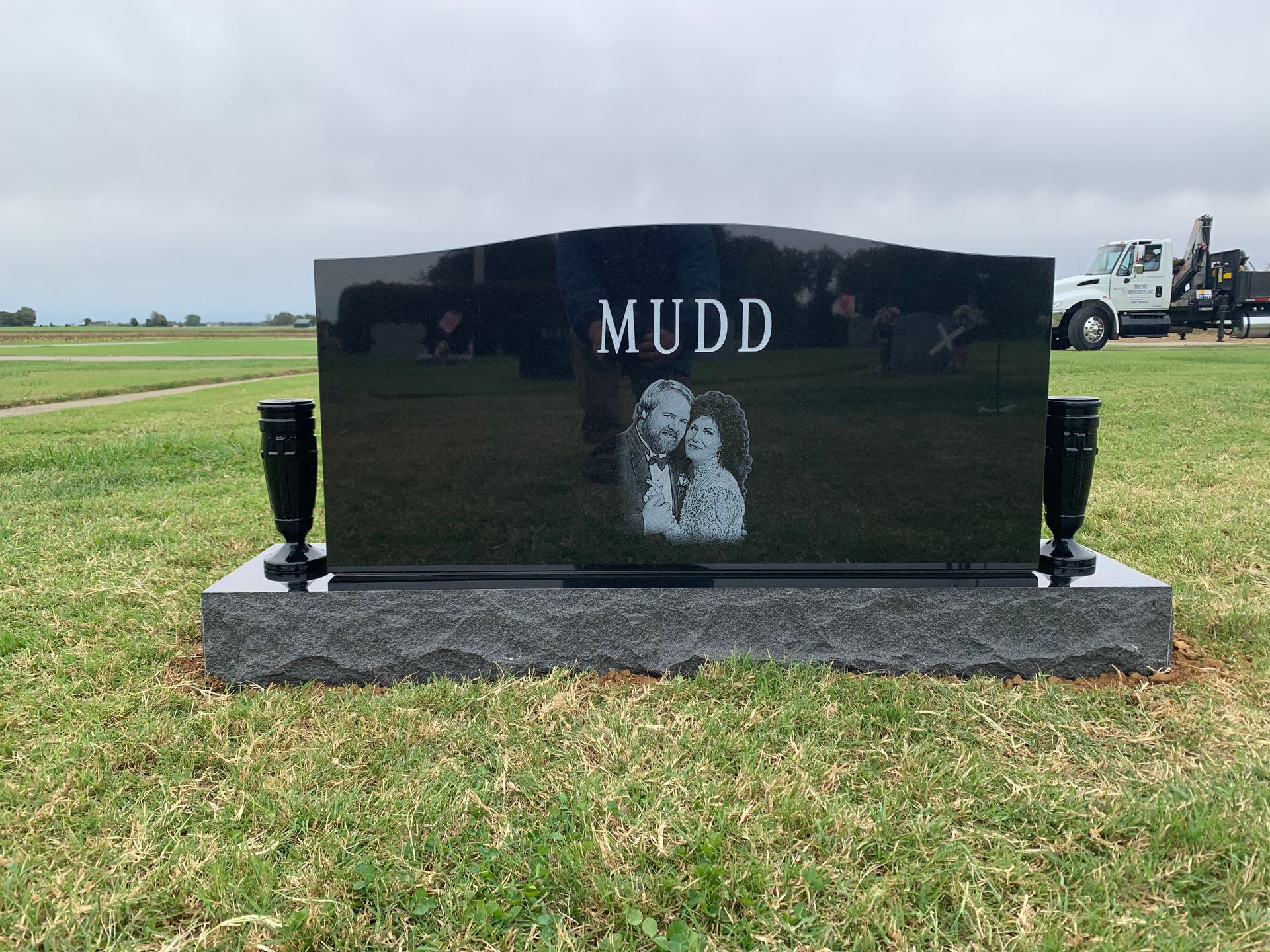 A black gravestone with the name mudd on it is in a grassy field.