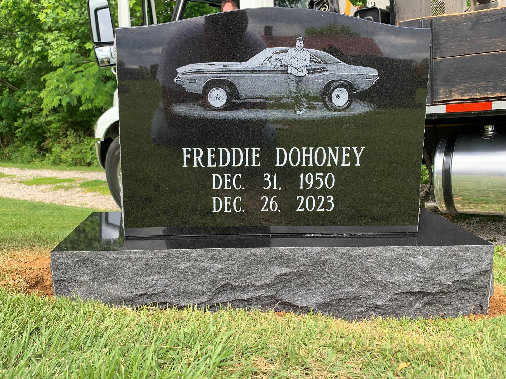 Black granite tombstone with a car graphic. It reads 