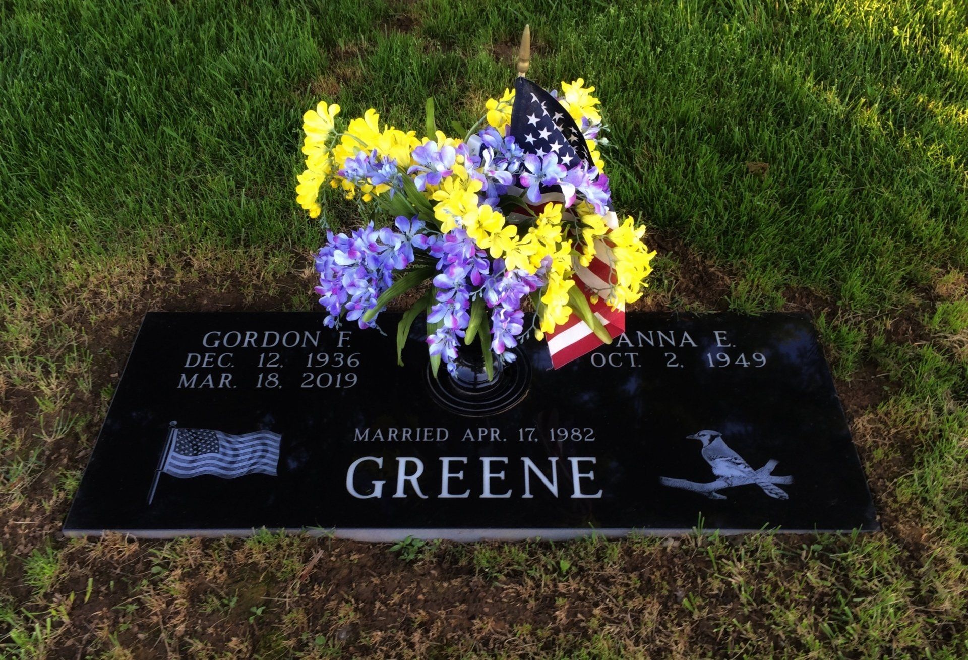 A gravestone for gordon greene with flowers and an american flag